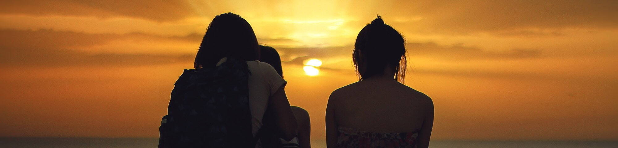 Three people sat watching beautiful sunset